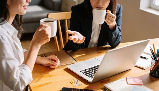Two asian professional women collaborating over coffee with laptop and notebooks