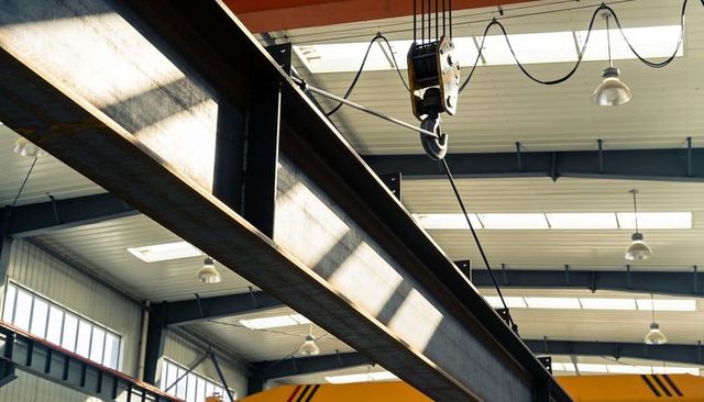 Rusty i-beam and overhead hoist in industrial workshop with skylights and steel structure