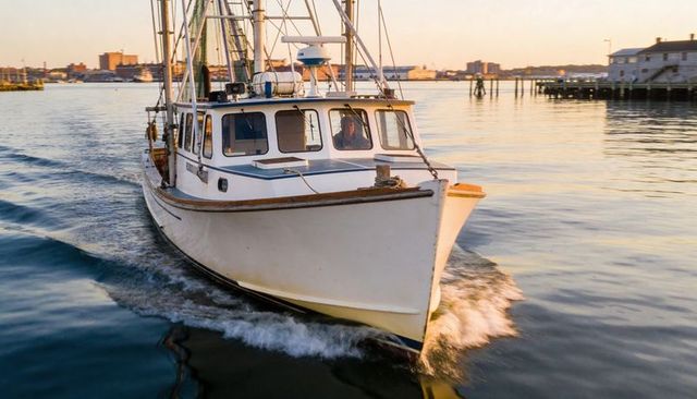 White fishing trawler heading toward camera in harbor at golden hour
