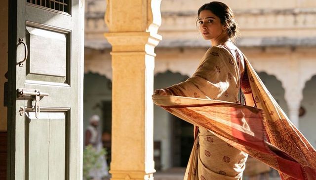 Indian woman holding flowing sari pallu and glancing back in sunlit heritage courtyard
