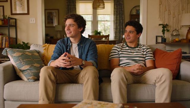 Two teenage males chatting on cozy living room sofa with cushions and macrame decor