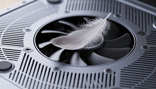 Pale feather resting on circular cooling fan highlighting delicate softness against metal