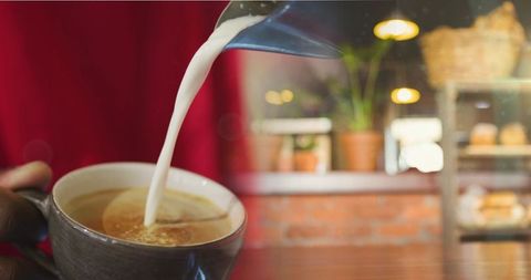 Barista Pouring Milk into Cappuccino in Cozy Cafe Setting