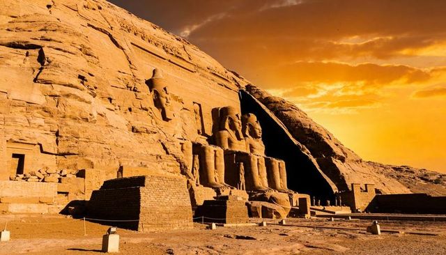 Ancient rock-cut temple bathing in sunset light with colossal seated statues, desert monument