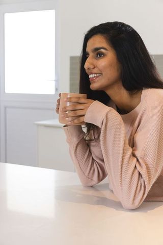 Smiling Indian Woman Sipping Tea at Bright Minimalist Kitchen Counter