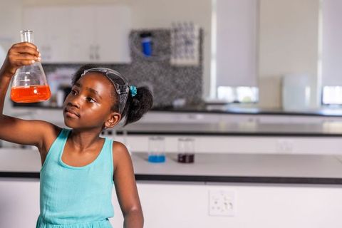 African american girl inspecting orange solution in school science lab wearing goggles