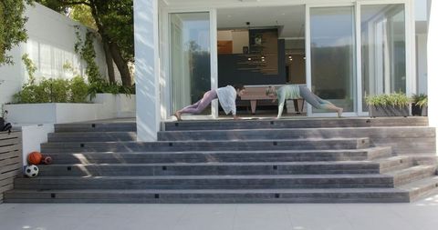 Two women holding plank pose on modern patio steps for outdoor home workout and core strength