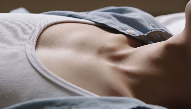 Reclining clavicle and neck close-up revealing delicate decolletage in open light-blue shirt