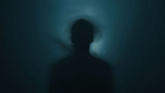 Silhouetted figure standing wearing dark clothing with halo backlight abstract portrait