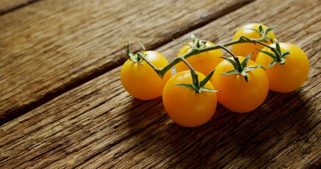 Bright yellow cherry tomatoes lying on a rustic wooden board. This image can be used in food blogs, recipe websites, or advertisements for organic and healthy produce. It emphasizes freshness and natural ingredients, making it ideal for culinary content and promoting healthy eating.