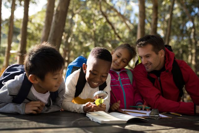 Teacher assisting diverse group of kids studying outdoors in a park. Children are engaged in learning with a magnifying glass and notebooks, showing curiosity and teamwork. Ideal for educational content, outdoor learning programs, and diversity in education themes.