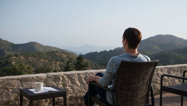 Man sitting on terrace overlooking hills with coffee and notebook, contemplative morning