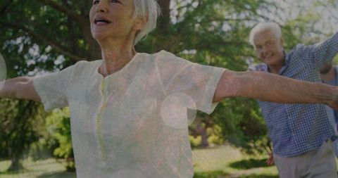 Active senior couple stretching in park under sunlit trees, joyful older adults outdoors