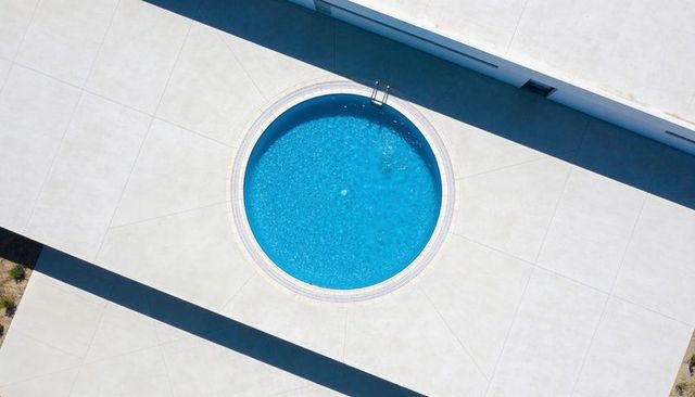 Circular rooftop pool on minimal concrete deck casting long diagonal shadows