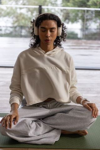 Nonbinary person meditating on wet veranda wearing headphones, smartwatch heart rate rings