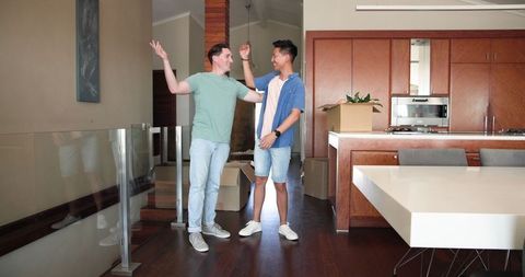 Happy diverse male couple moving into new home with boxes