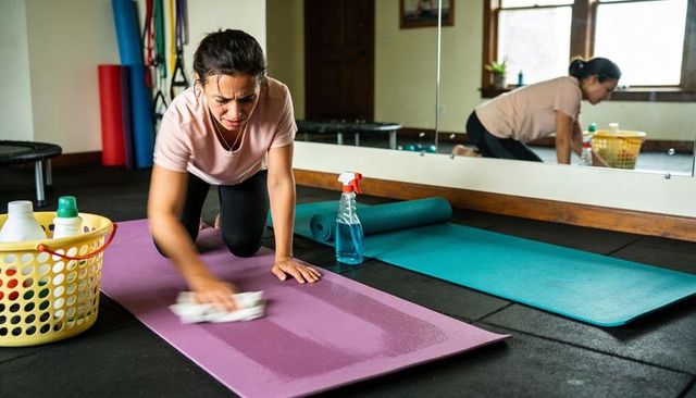 Vigorous woman wiping yoga mat in home gym cleaning workout space and fitness equipment