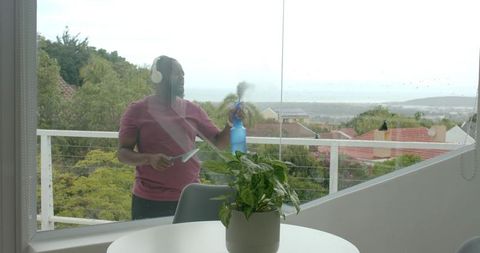 African man cleaning balcony glass with spray bottle and squeegee overlooking bay