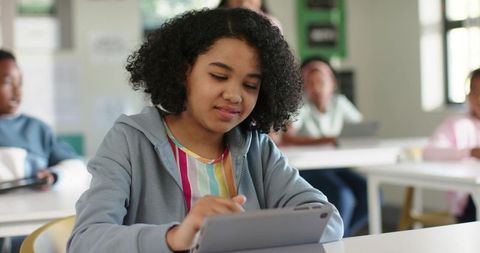 African American girl using tablet in modern classroom with peers learning digitally