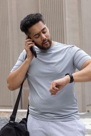 African american man checking watch while talking on phone with duffel bag