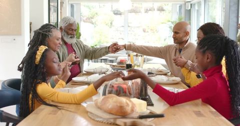 Multigenerational Family Holding Hands Giving Thanks Around Wooden Dining Table