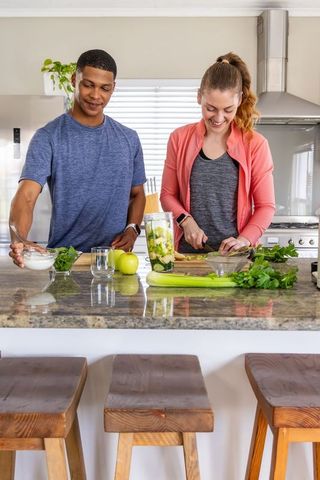 Couple preparing green smoothie ingredients together at bright modern kitchen island
