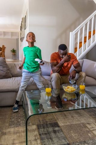 Joyful african american boy celebrating victory while father reacting during home gaming