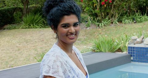 Indian woman smiling by pool wearing white crochet coverup and hoop earrings