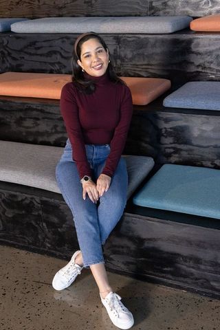 Young woman sitting smiling on tiered bench in modern coworking lounge with smartwatch