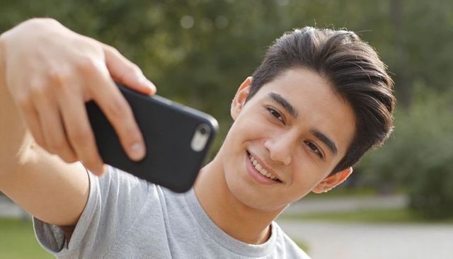 Teen taking selfie outdoors with smartphone smiling in green park