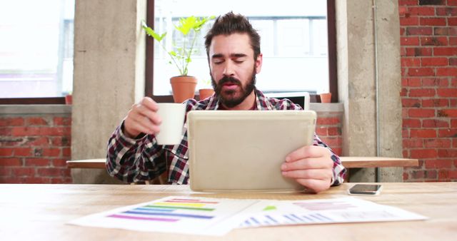 Man Drinking Coffee while Using Tablet at Work Desk in Modern Office - Download Free Stock Images Pikwizard.com