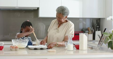 African american grandmother baking with granddaughter in modern kitchen, sharing recipe