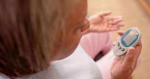Senior woman checking blood glucose with glucometer at home