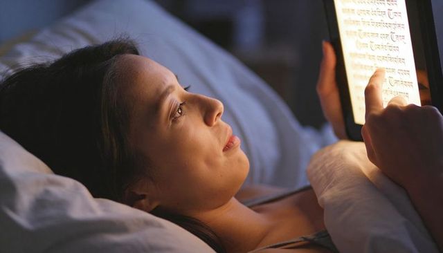 Young woman reading tablet in bed at night with devanagari script and warm bedside glow
