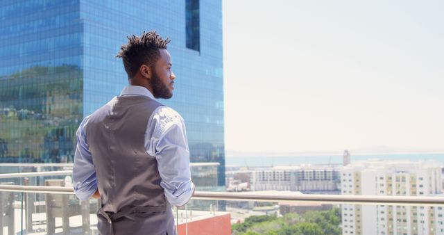Businessman in vest and formal wear standing on rooftop terrace, overlooking modern city skyline. Great for business themes, corporate imagery, success stories, urban lifestyle, modern work environment, professional thinking and goal-setting visuals.