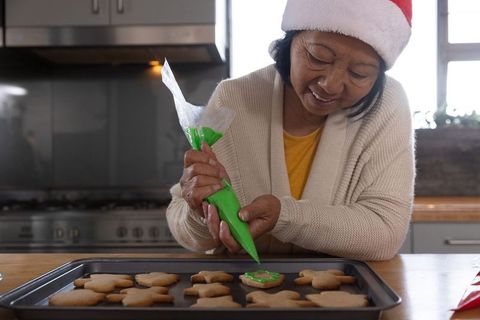Joyful elderly woman baking festive cookies with green icing