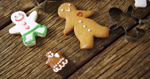 Gingerbread cookies in various sizes lie next to cookie cutters on a wooden surface, with copy space. These festive treats are often associated with holiday traditions and baking activities.
