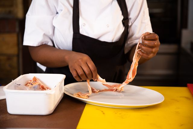Front view mid section of an African American working in a restaurant kitchen, holding rashers of bacon, lying it on a plate 