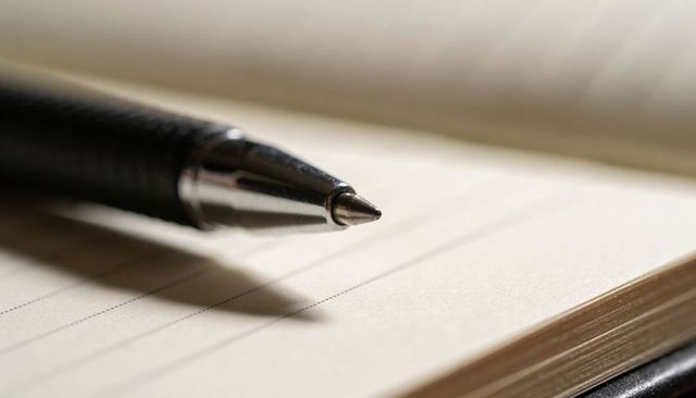 Macro close-up black ballpoint pen tip resting on cream lined notebook for journaling