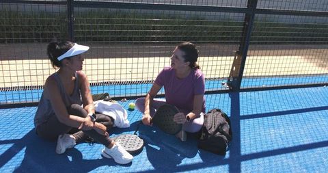 Women chatting and relaxing on blue padel court after match, casual sports break