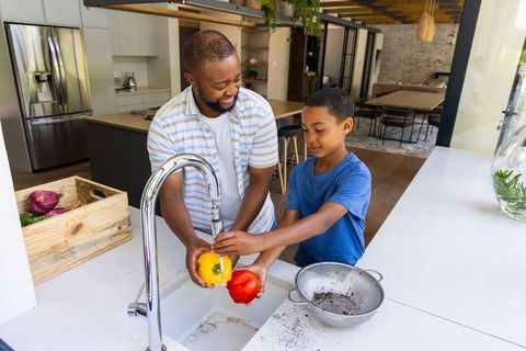 African american father and son washing bell peppers together in bright open-plan kitchen