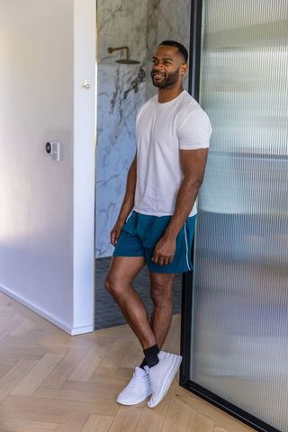 African american man leaning at frosted glass door in minimalist home in tee and shorts