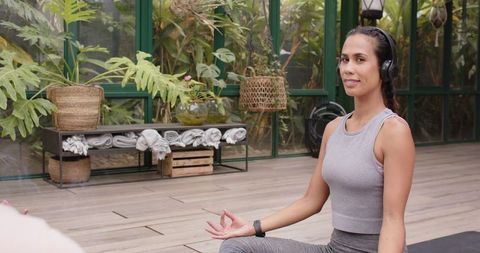 Woman Meditating with Headphones in Serene Glass House Garden