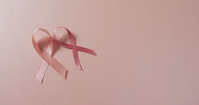 Two pink ribbons on a pastel pink background symbolizing breast cancer awareness. Ideal for healthcare campaigns, nonprofit fundraising materials, awareness event promotions, and educational materials about the importance of early detection and prevention of breast cancer.