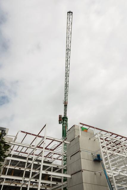 Crane towering over construction site with steel framework and concrete structures. Ideal for illustrating themes of urban development, industrial progress, and construction engineering. Useful for articles, presentations, and marketing materials related to construction projects, architecture, and infrastructure development.