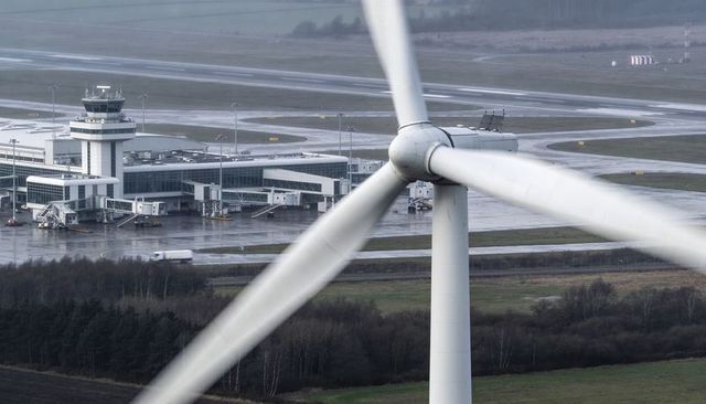 Wind turbine dominating airport terminal with rotating blades, wet runways, control tower