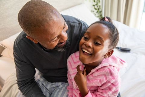 African american father laughing with daughter in pink robe sharing cozy morning hug