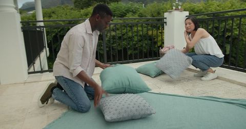 Diverse couple setting up cozy terrace picnic for celebration