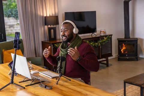 African american man live streaming from livingroom with laptop, microphone, headphones