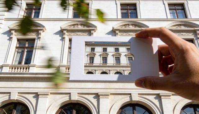 Holding card frame over neoclassical facade with ornate windows, arches and decorative cornices